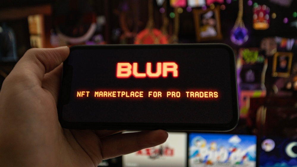 A man holds an iPhone XR showing the logo of NFT marketplace Blur