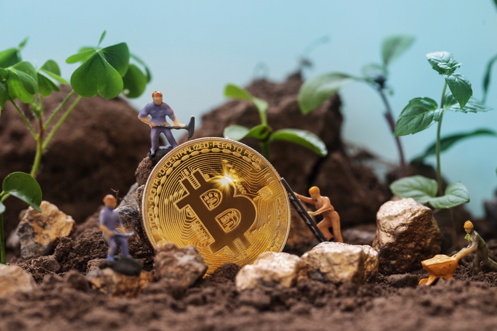 Renewable Cryptocurrency Mining. Miner figurines digging ground to uncover big Gold bitcoin.