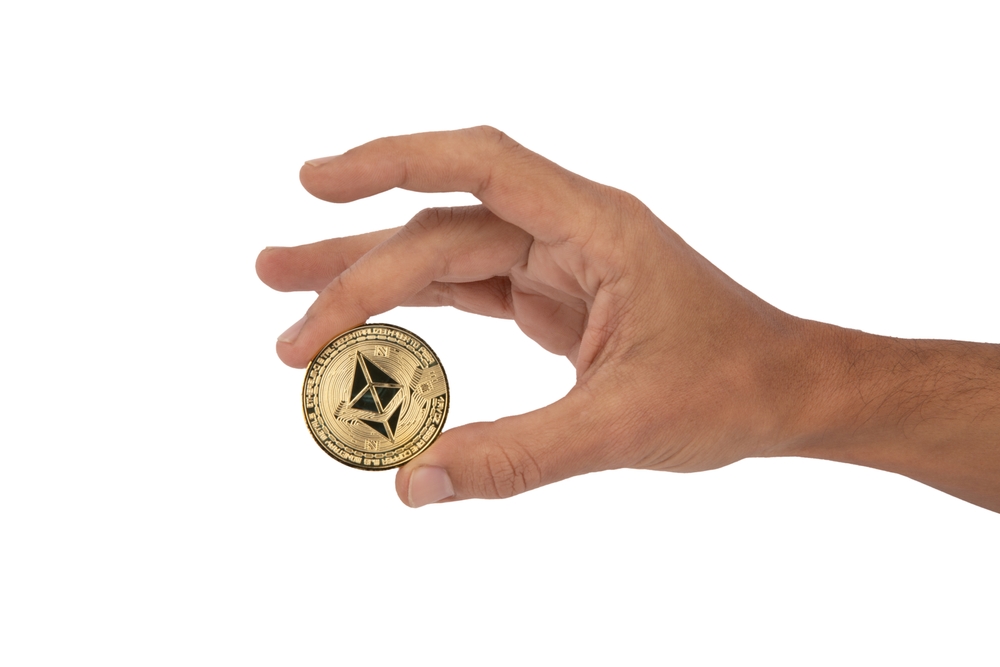 Hand holding with its fingers a golden ethereum token
