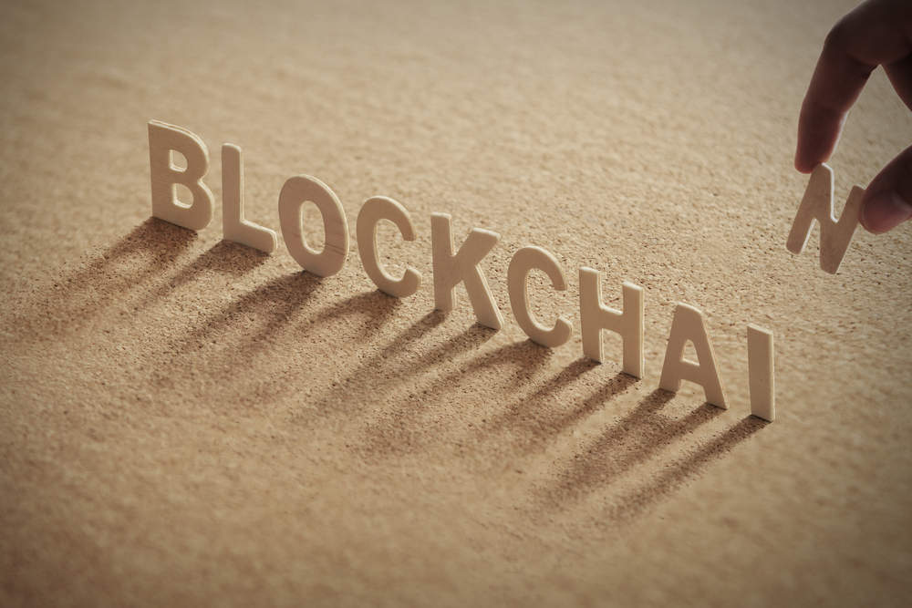 BLOCKCHAIN wood word on compressed or corkboard with human's finger at T letter.