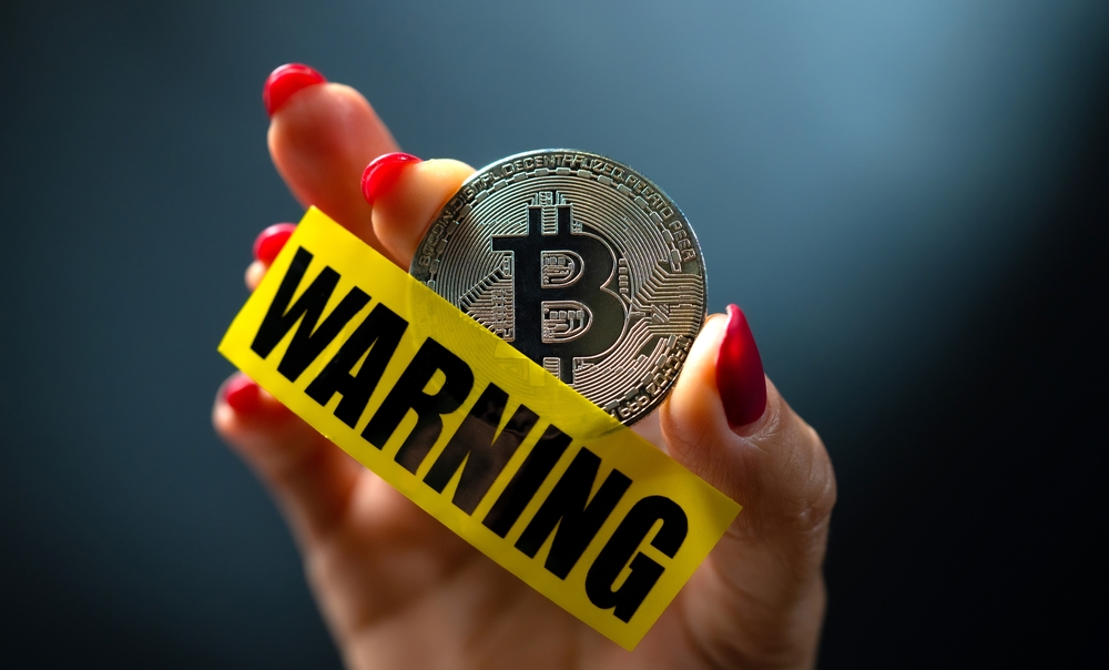 Hand holding bitcoin virtual currency coin and yellow caution tape with word warning.
