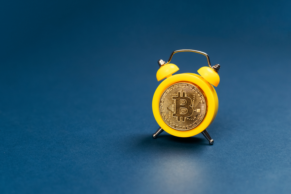 Concept deadline to invest in cryptocurrency showing alarm clock with a bitcoin as the clock face on blue background.