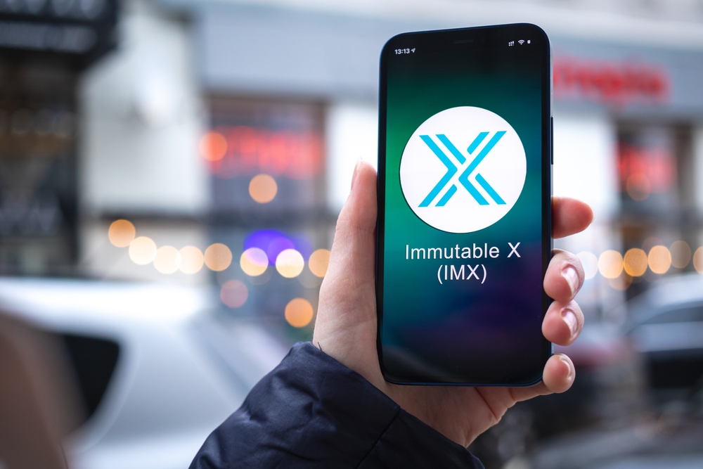 Immutable X IMX coin symbol. Trade with cryptocurrency, digital and virtual money, mobile banking. Hand with smartphone, screen with crypto icon close-up