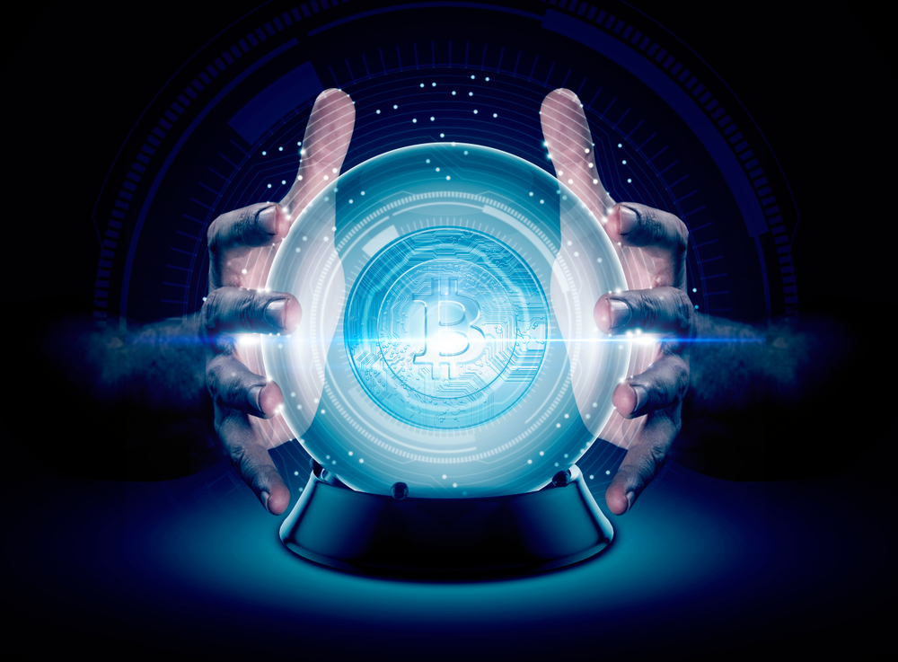 A pair of male hands surrounding a crystal ball conjuring up a bitcoin crytocurrency hologram on an isolated dark studio background