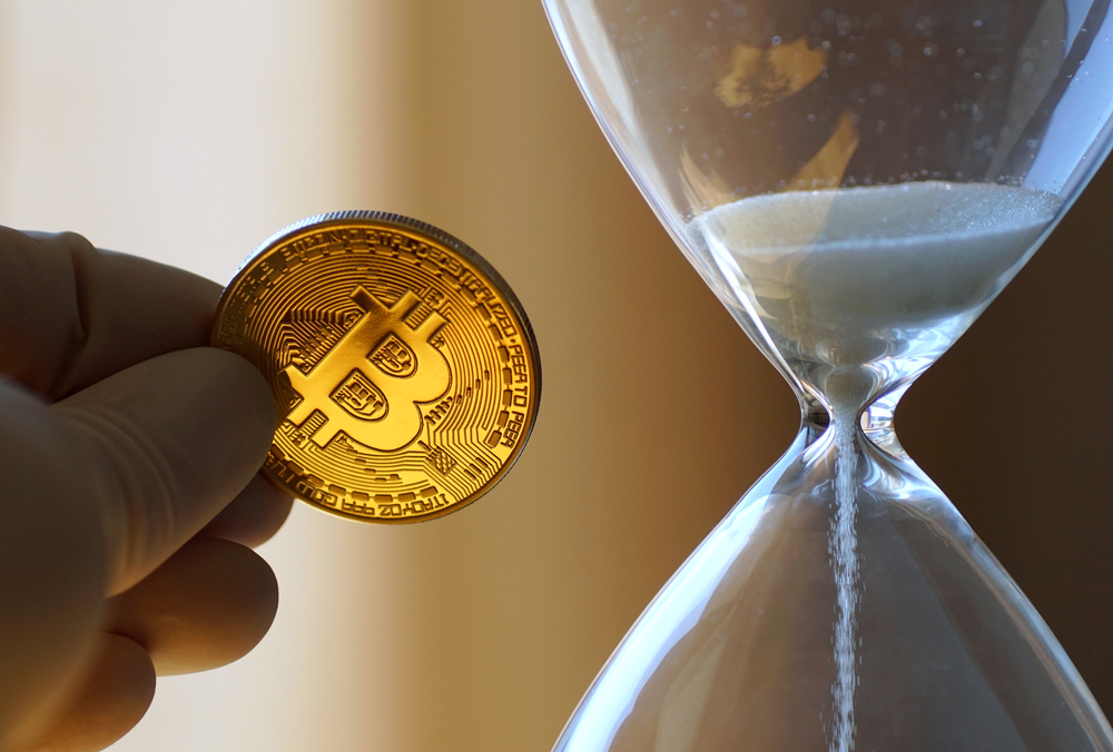 Holding a golden BTC coin in front of a hourglass