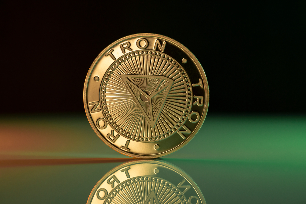 Tron TRX cryptocurrency physical coin placed on reflective surface and lit with green and red lights