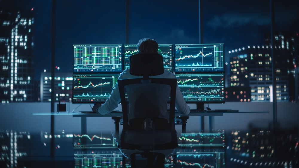 Financial Analyst Working on Computer with Multi-Monitor Workstation with Real-Time Stocks, Commodities and Exchange Market Charts.