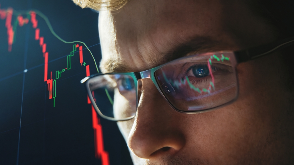 Close-up portrait of focused crypto trader analyst wearing eyeglasses looking at computer screen analyzing stock market charts