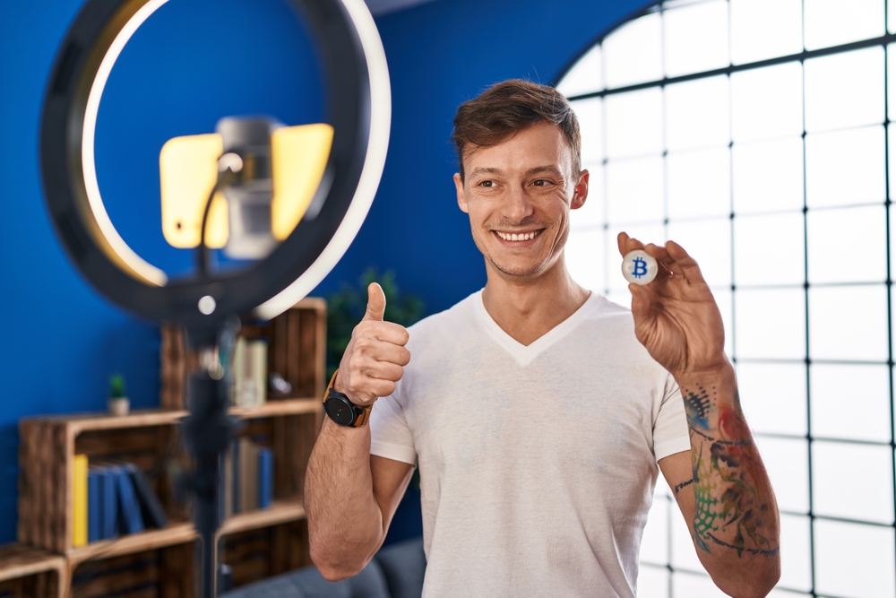 Caucasian man recording bitcoin tutorial with smartphone at home smiling happy and positive, thumb up doing excellent and approval sign