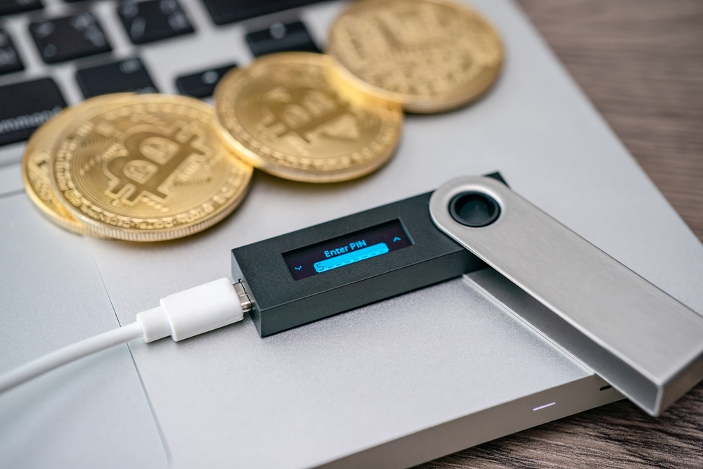 Hardware cryptocurrency wallet with golden Bitcoin (BTC) on computer. Safe storage for crypto.