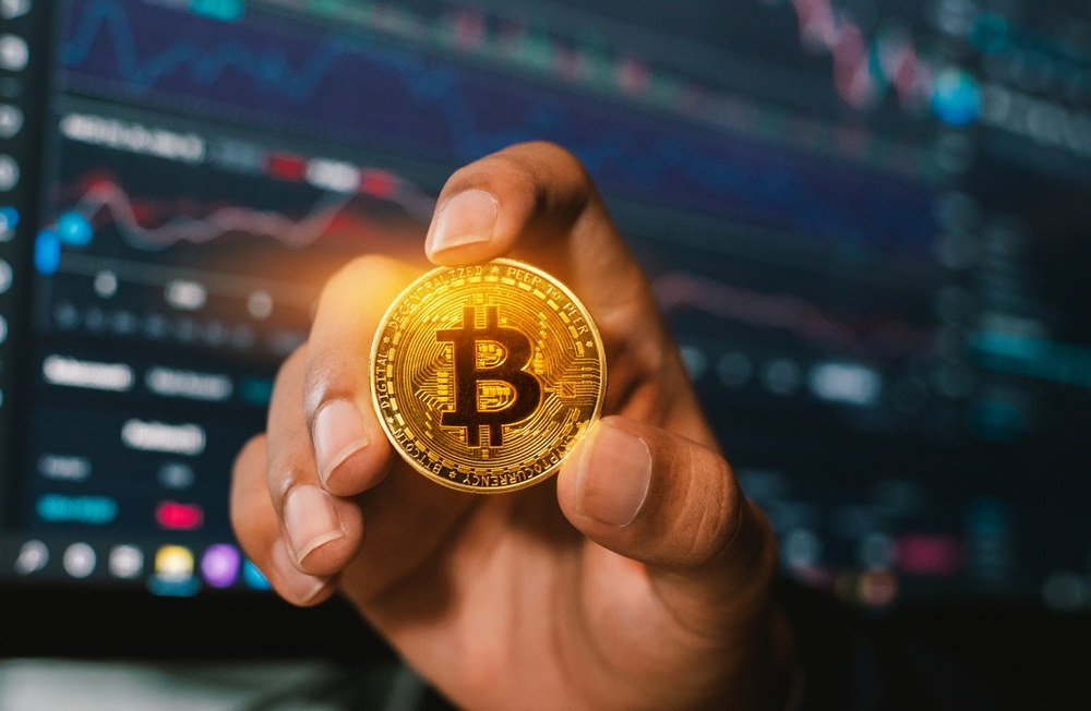 a man holding golden coins with bitcoin symbol and crypto trading graph in background