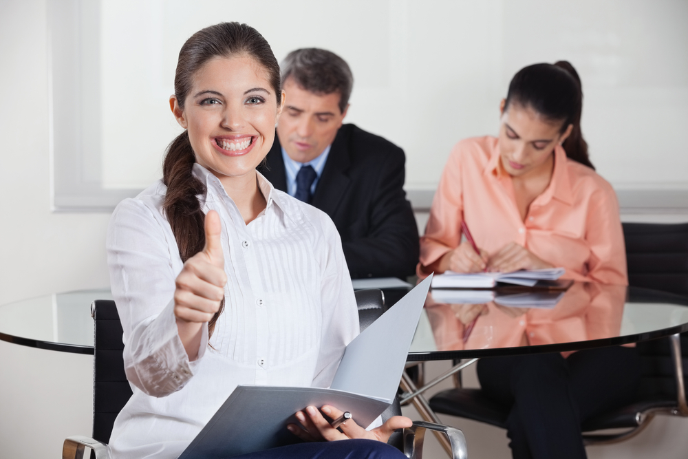 Happy busines woman with files in office holding her thumbs up