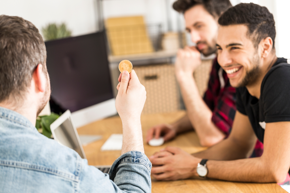 Smiling man looking at friend with gold BitCoin - symbol of digital money