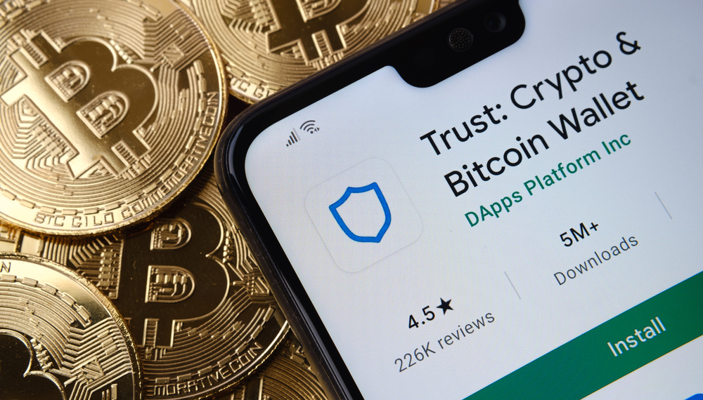 Trust Crypto Bitcoin Wallet app seen on the smartphone screen placed on top bitcoin coins pile.