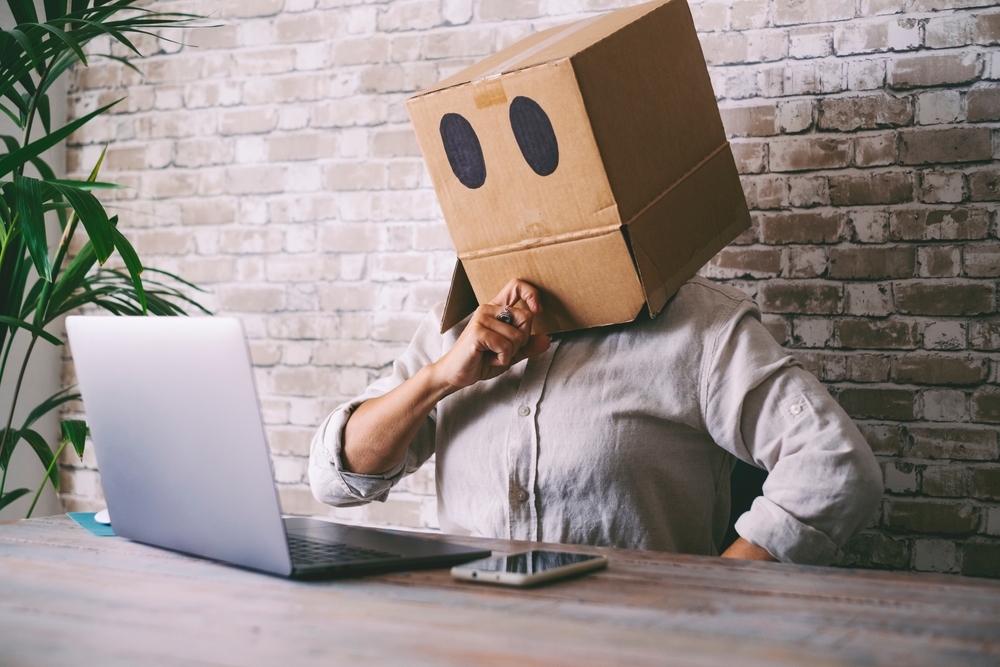 Home worker with paper box on his head. Anonymous people use laptop computer. Concept of doubts and problems with privacy online web protection. Communication and connection online