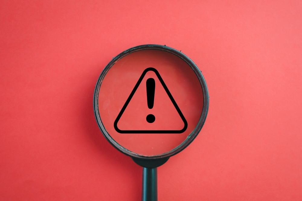 View through a magnifying glass on Exclamation mark or Warning sign over red background Attention sign,Exclamation mark,warning sign concept.