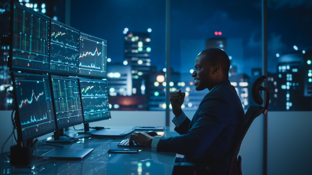 Stock Market Day Trader Working on Computer with Multi-Monitor Workstation with Real-Time Investmentment Charts.