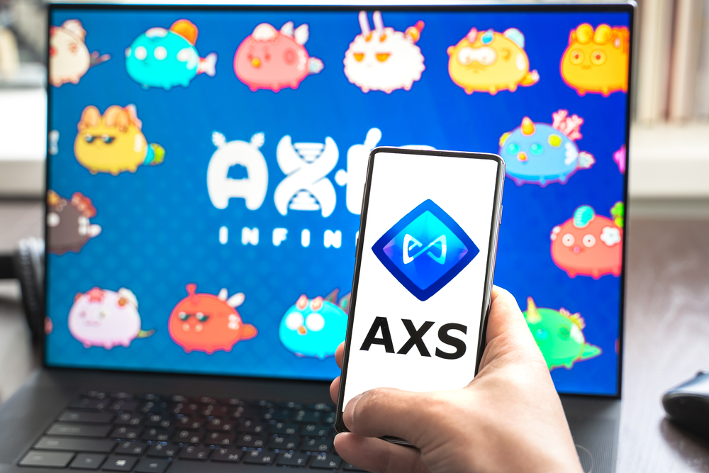 .Logo,screenshot of blockchain nft ethereum cryptocurrency game Axie in laptop,mobile phone.Man playing,collecting,creating crypto pet,heroes. Earning digital money tokens AXS.