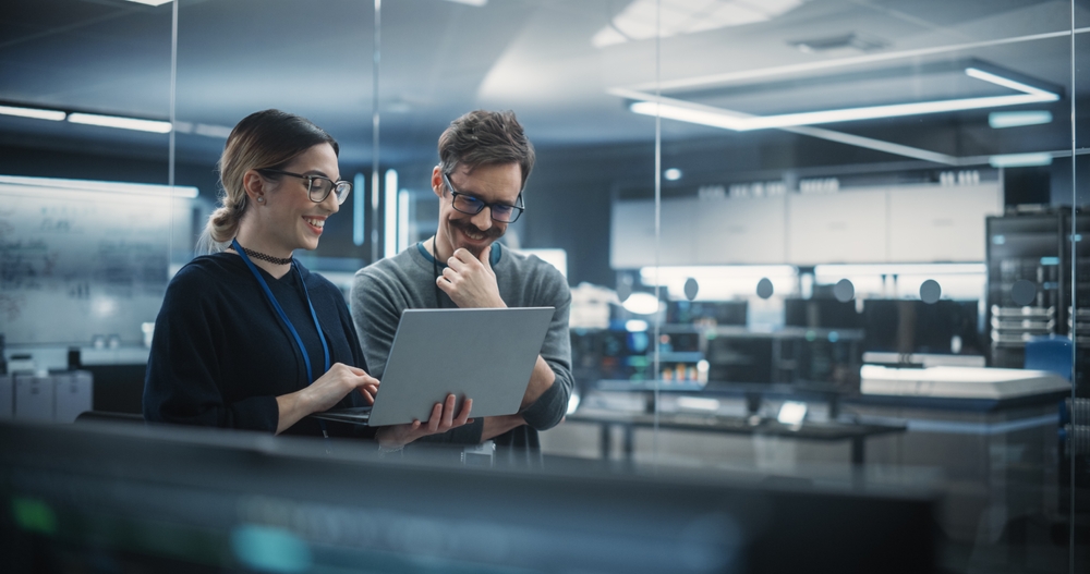 Portrait of Two Creative Young Female and Male Engineers Using Laptop Computer to Analyze and Discuss How to Proceed with the Artificial Intelligence Software.