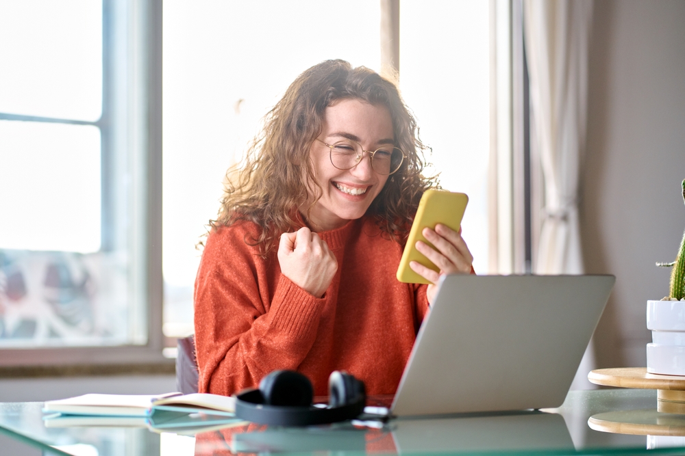 Young happy lucky woman student feeling excited winner looking at cellphone using mobile phone winning online, receiving great news or sms offer, getting new job celebrating achievement.