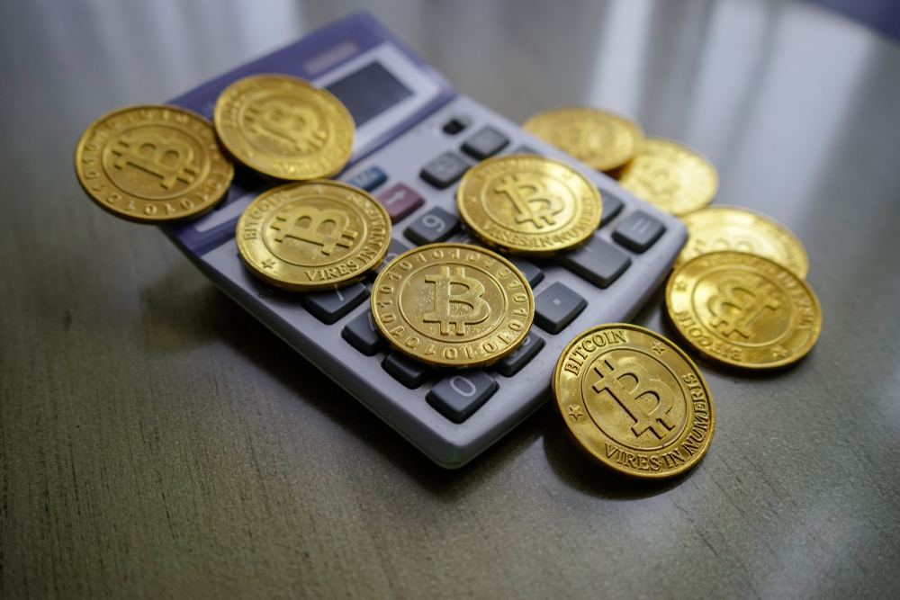 Golden bitcoin with calculator on wooden table as background. Fees and taxes on cryptocurrency investments