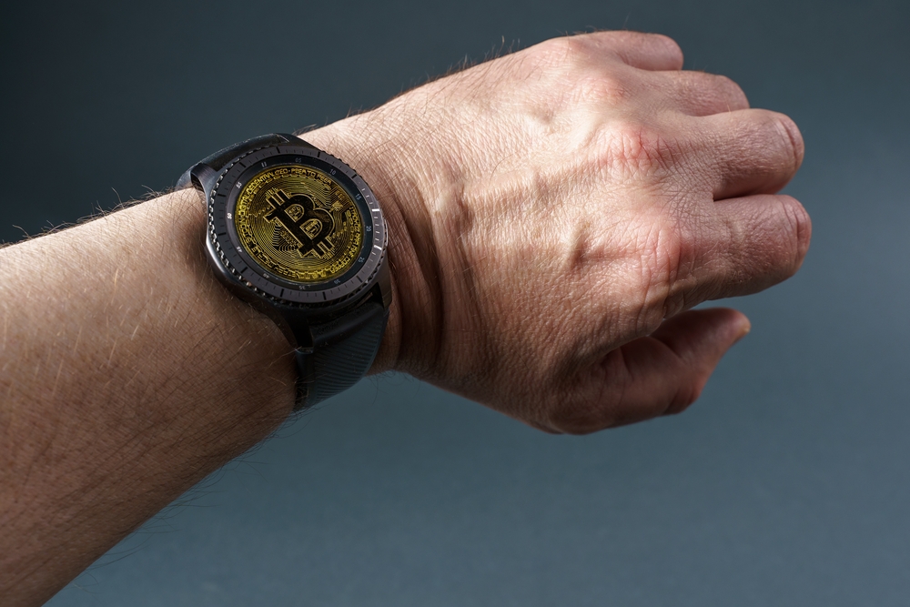 Smart watch with a bitcoin screen on a man's hand, close-up on a gray background. 