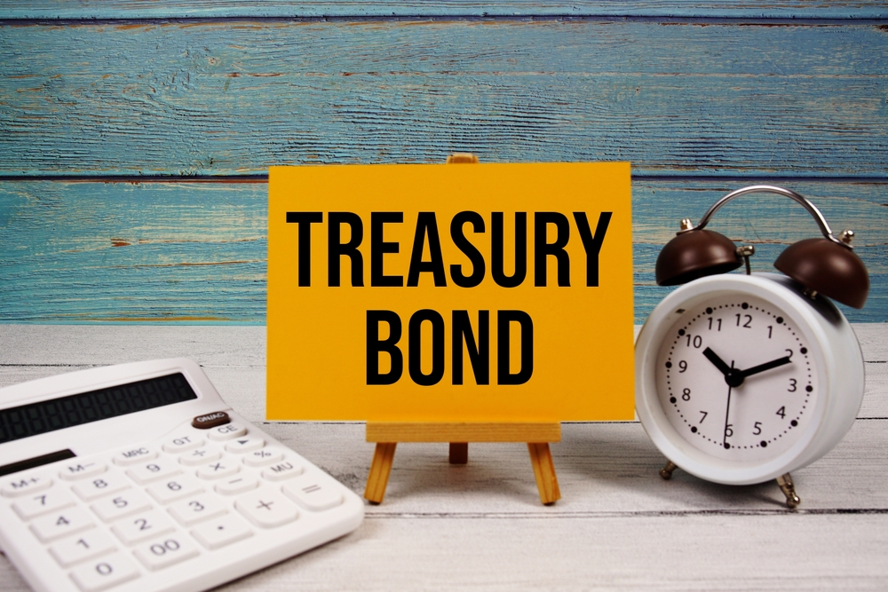 Treasury Bond text written on paper card with calculator and alarm clock on wooden background